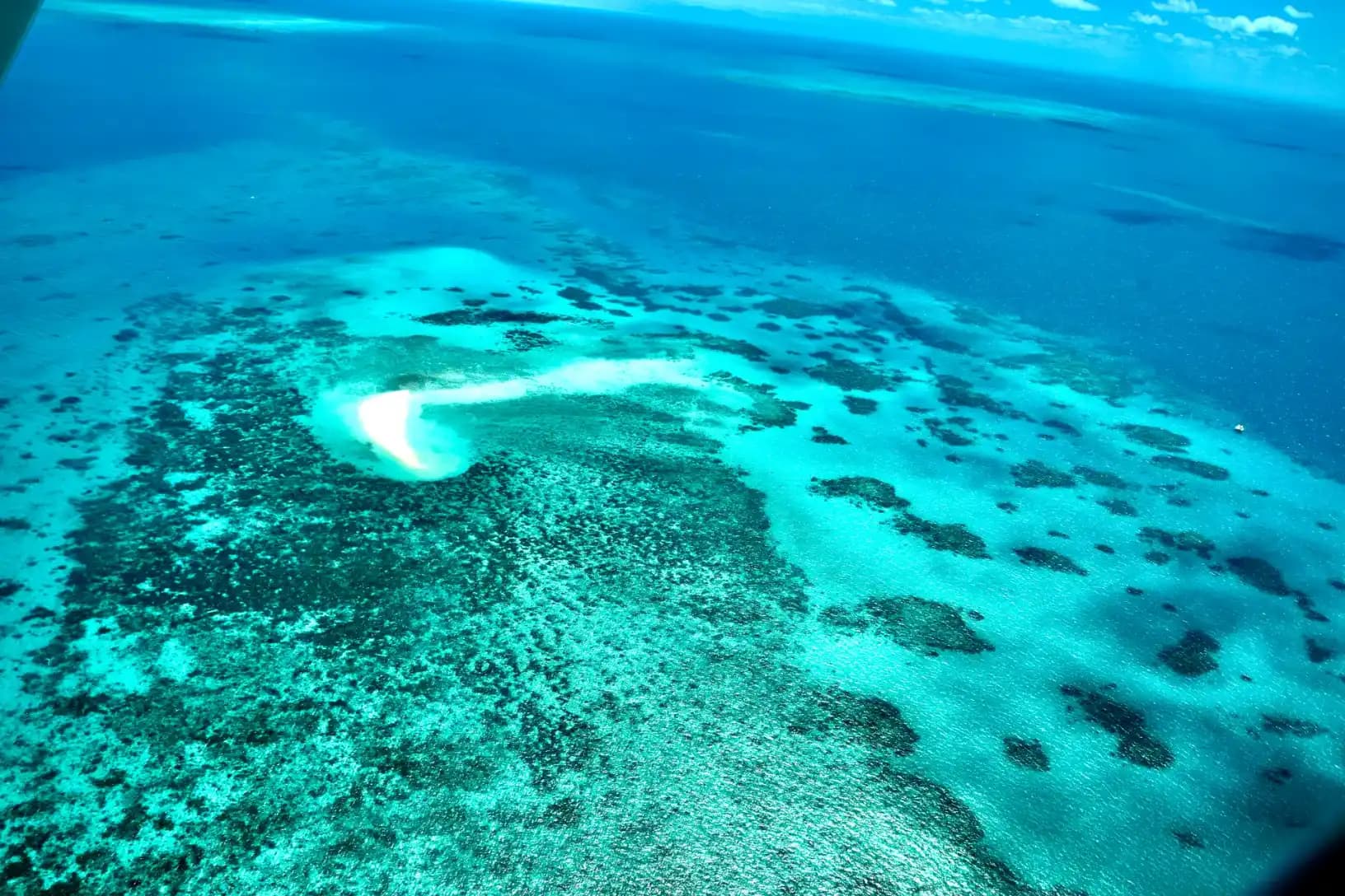 Aerial view of the Great Barrier Reef showing turquoise waters, coral formations, and a white sand cay off the Queensland coast