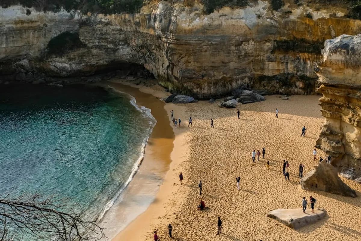 Aerial view of Loch Ard Gorge beach with turquoise water and visitors on golden sand