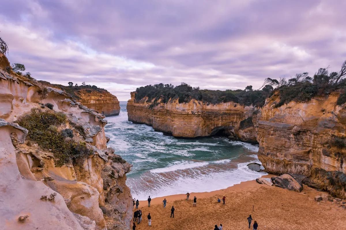 Looking through Loch Ard Gorge from beach level with visitors and purple evening sky