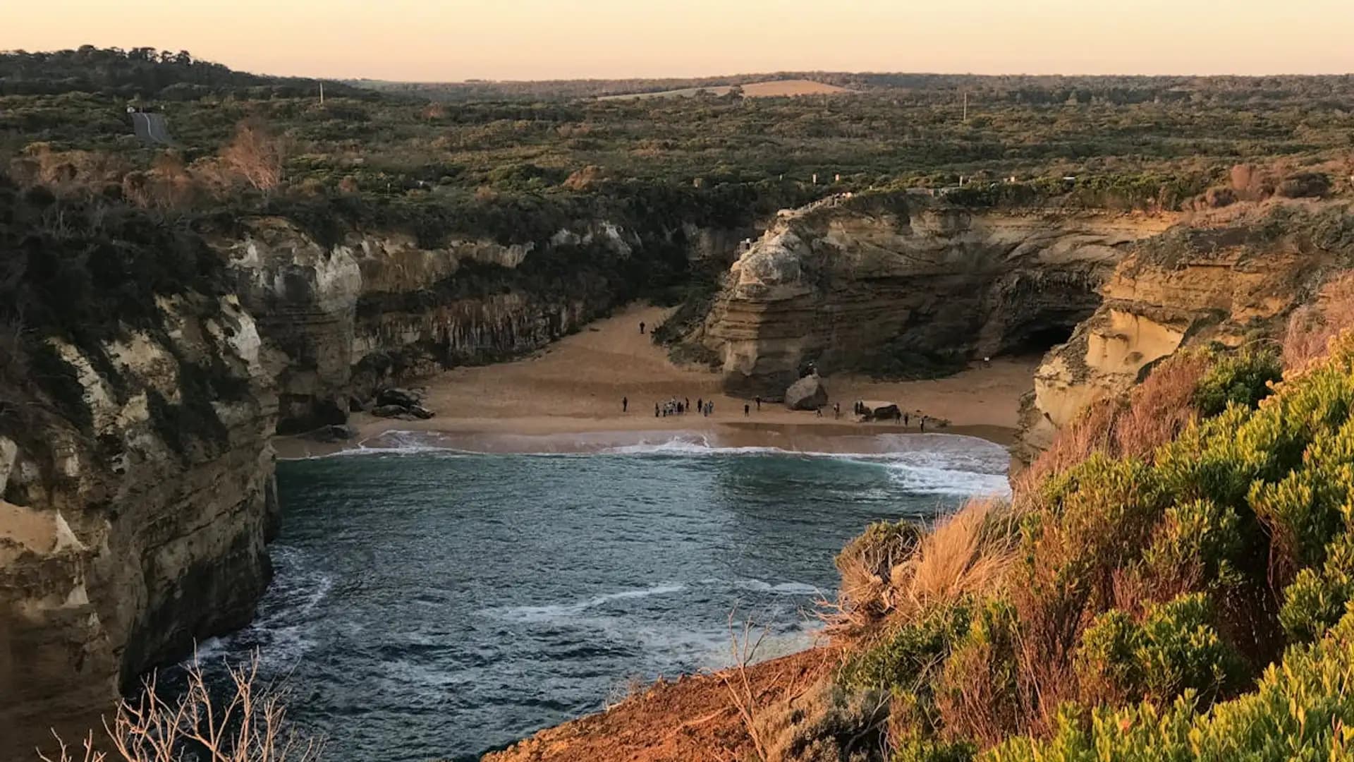 Loch Ard Gorge viewed from the clifftop lookout at golden hour with visitors on the beach below