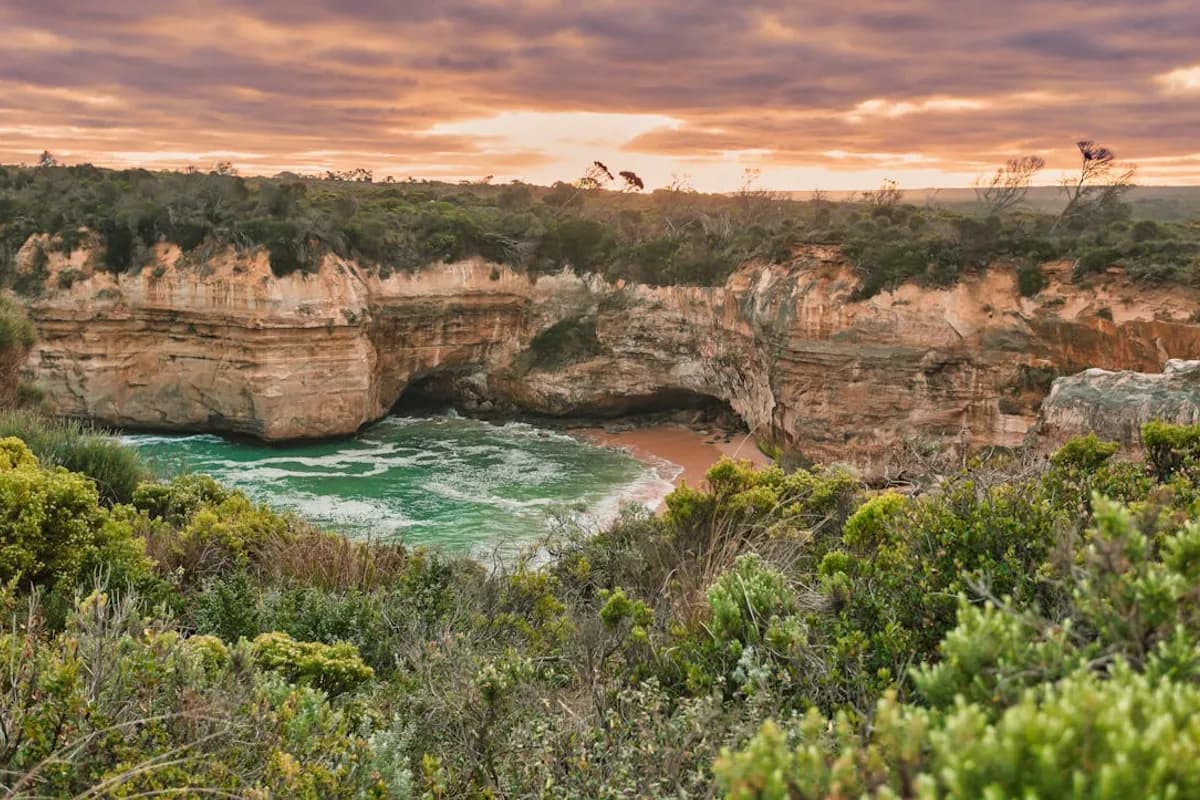 Loch Ard Gorge at sunset framed by coastal scrub with dramatic pink and orange sky