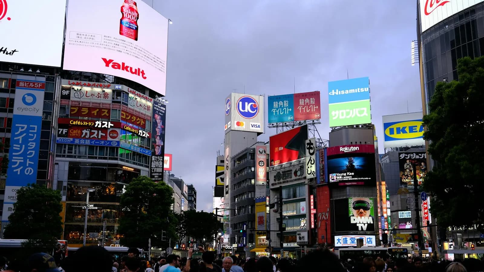 Tourists and locals crossing Shibuya in Tokyo at dusk, the worldʼs busiest pedestrian crossing, moving quietly and in order.
