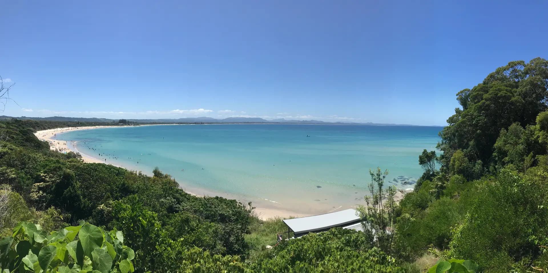Panoramic view of Byron Bay beach with turquoise water and white sand backed by the Cape Byron headland